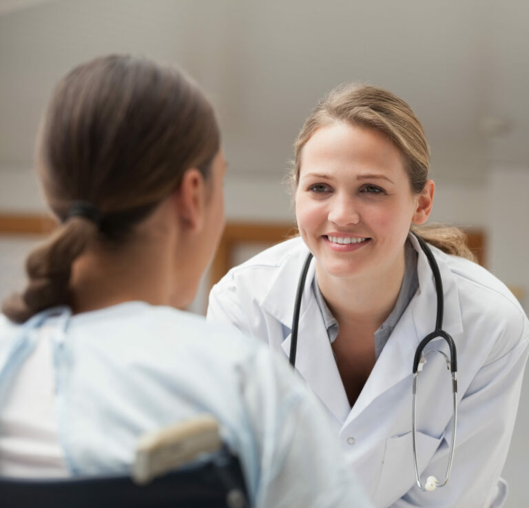 Smiling doctor looking at a patient on a wheelchair in hospital hallway