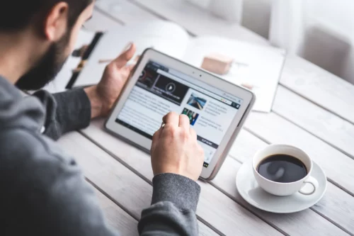 man looks at a digital tablet and reads the news with a cup of coffee next to him