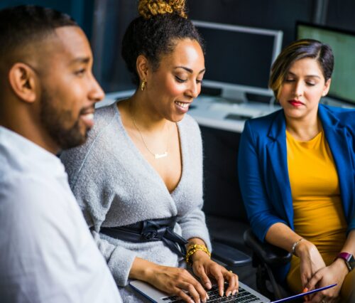 woman on a computer sitting with another woman and a man