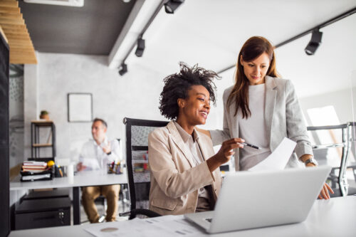 two women consult at a laptop