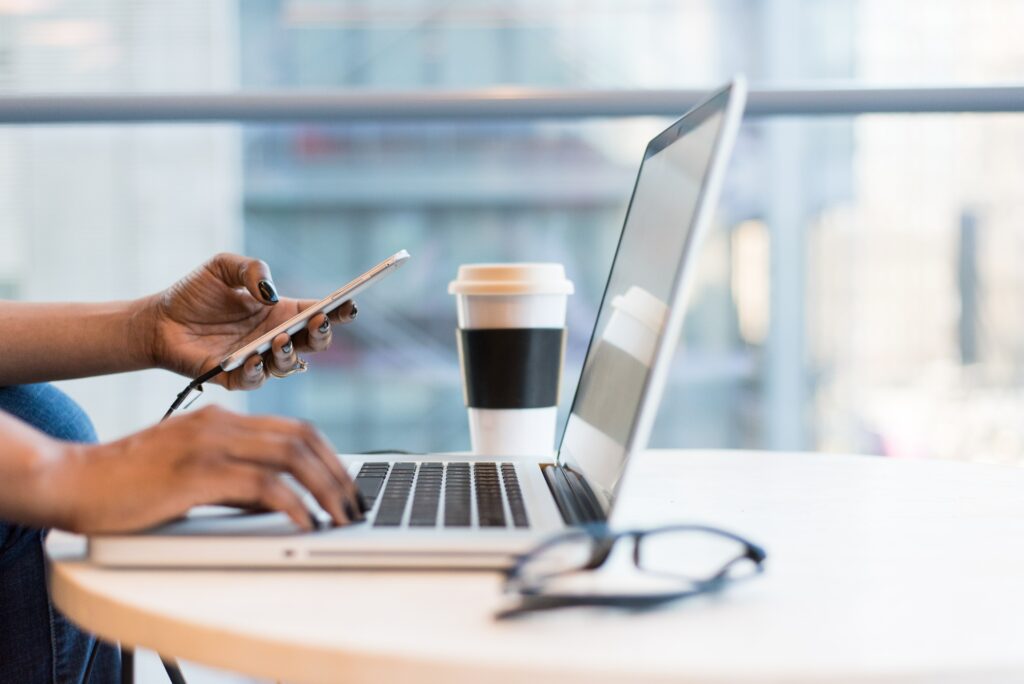 person working at a laptop while typing on phone in a glass office