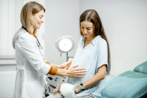 Young pregnant woman sitting on the gynecological chair during a medical consultation with gynecologist. Cheerful doctor supporting and comforting patient