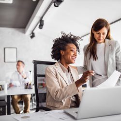 two women consult at a laptop