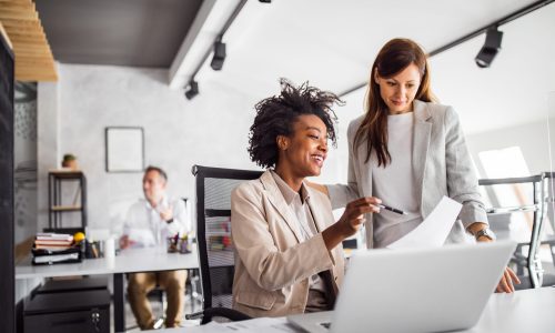 two women consult at a laptop