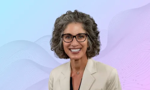 Portrait of a smiling woman with short gray hair and tortoiseshell glasses, wearing a beige blazer.