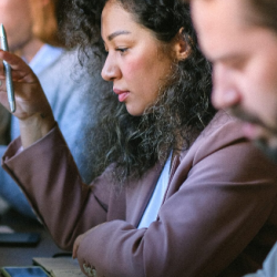 woman in middle distance looks at computer and holds pen, man in foreground and background