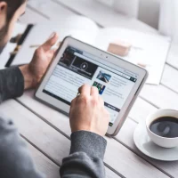 man looks at a digital tablet and reads the news with a cup of coffee next to him