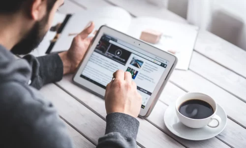 man looks at a digital tablet and reads the news with a cup of coffee next to him