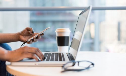 person working at a laptop while typing on phone in a glass office