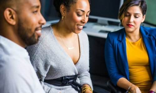 woman on a computer sitting with another woman and a man