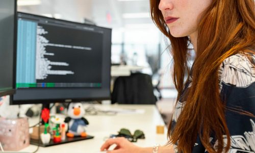 woman with red hair looking at a computer monitor